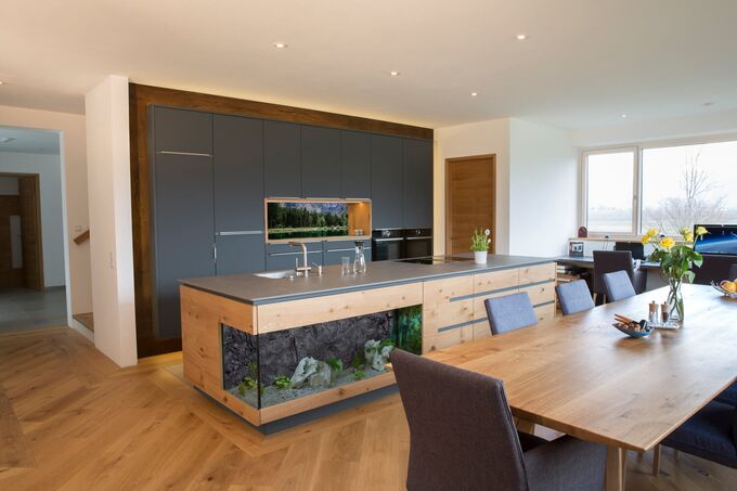 Großzügige Kücheninsel in Eiche mit Aquarium, Bora Dunstabzug, Keramikarbeitsplatte, Hochschränke in grauem Dekor und Nischenrückwand