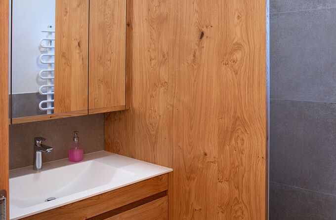 Ein kleines Badezimmer in Eiche mit Blick auf einen Waschtisch, Spiegelschrank und die Duschtrennwand